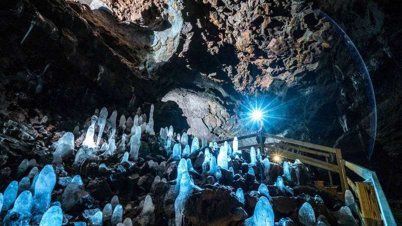 Viðgelmir Lava Cave in the wintertime with stalagmites raising from the ground lighten up by a phone torch