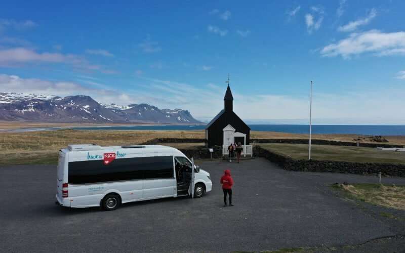Black Church with mountains and the ocean in the background and Nicetravel bus in the front