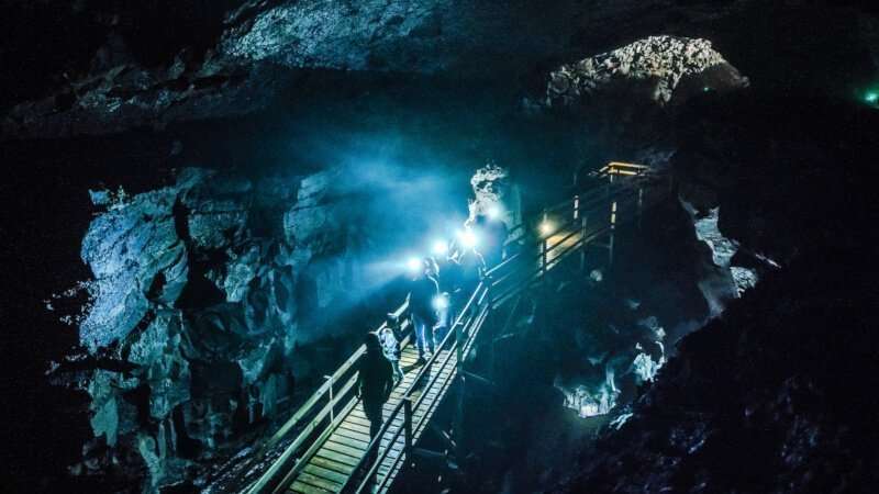 Inside the lava cave, people with headlamps descending the path