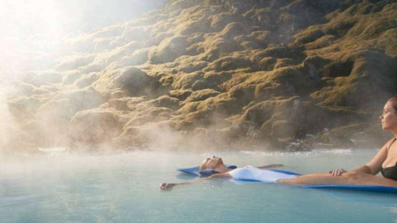 Blue lagoon, people chilling in the water on a sunny day with mossy hills