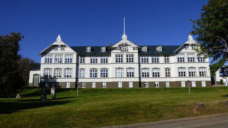 White building in Akureyri with grass and ble sky