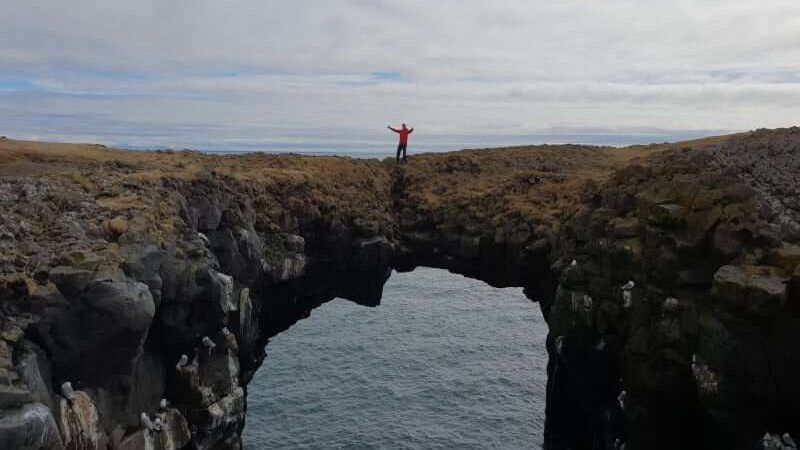 Arnarstapi - person standing on a stone arch above the ice cold water