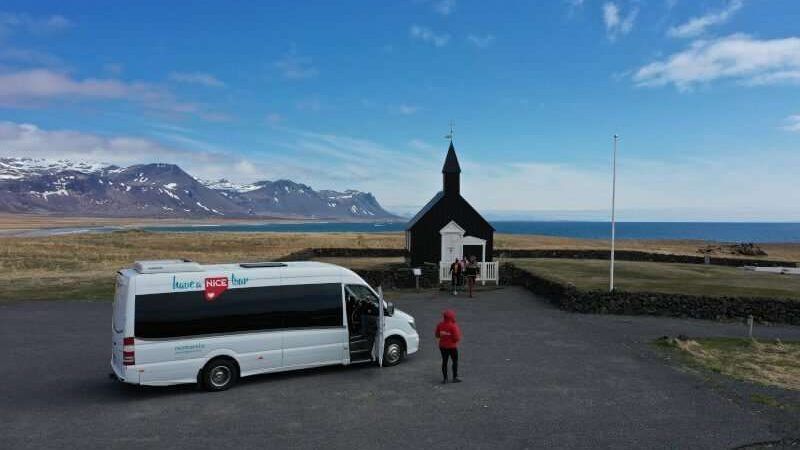 Black Church with mountains and the ocean in the background and Nicetravel bus in the front