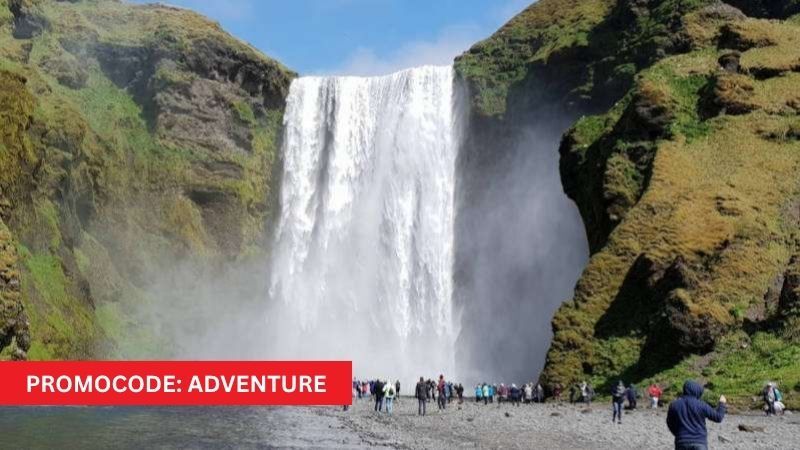 Skógafoss waterfall in Iceland on a sunny day with plenty of people with promocode ADVENTURE